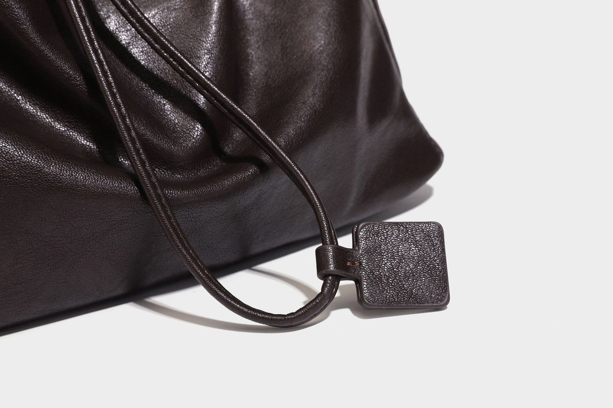 Lässig fallende Beuteltasche mit Kordelzug in dunkler Espresso-Lederoptik, verstellbarem Riemen und Ringbeschlägen aus Metall