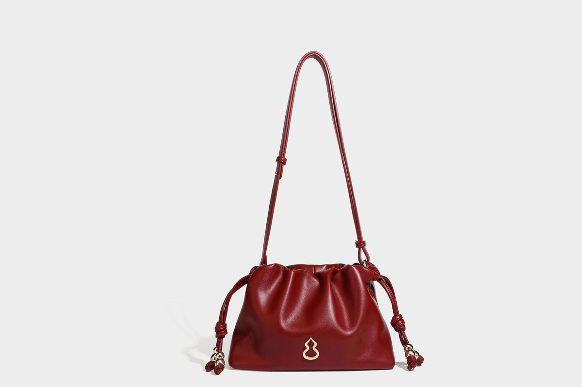 Slouchy ruched drawstring shoulder bag in smooth leather-look finish with gold-tone emblem and slim adjustable strap, detail
