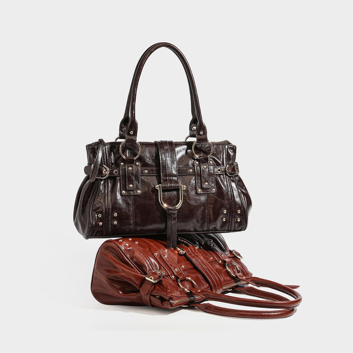 Dark brown glossy leather-look structured satchel tote with gold-tone studs, buckle straps, dual top handles, and detachable