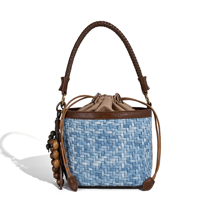 Small light blue woven bucket bag with brown leather-look trim, braided top handle, brass-tone ring hardware, drawstring