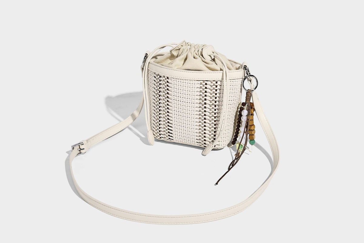 Small woven bucket bag with drawstring top, braided handle, detachable crossbody strap, and silver-tone ring hardware, detail