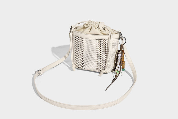 Small woven bucket bag with drawstring top, braided handle, detachable crossbody strap, and silver-tone ring hardware, detail