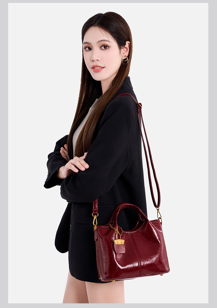 Structured crinkle-gloss top-handle satchel in deep burgundy with antique gold lock charm and detachable shoulder strap