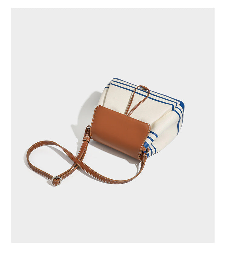 Cream canvas bucket bag with blue horizontal stripes, tan leather-look flap and trim, drawstring closure, silver-tone, detail