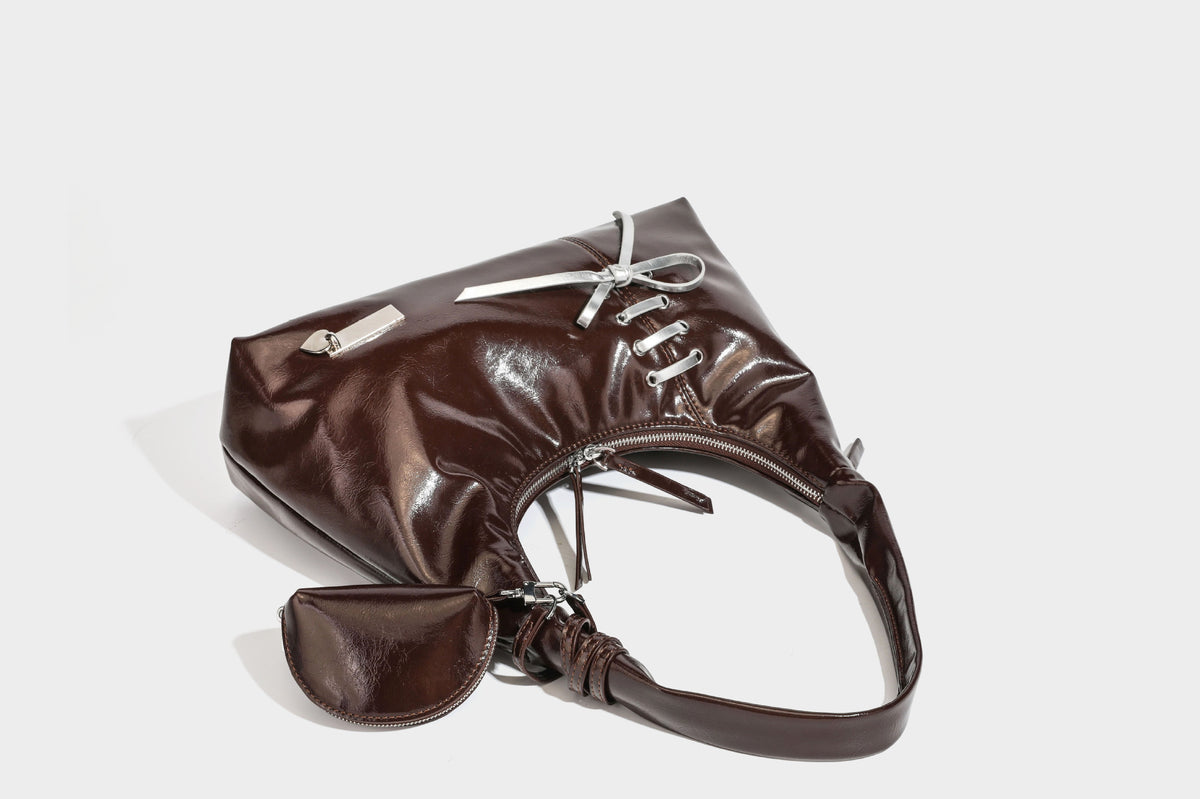 Weich fallende Hobo-Schultertasche in glänzender Lederoptik mit silberfarbenen Ösen zum Schnüren und Schleifenband auf der Vorderseite, Detailansicht