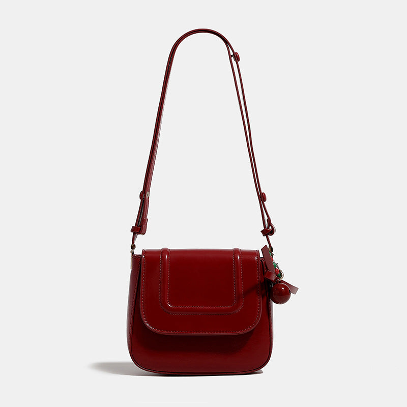 Mini glossy leather-look saddle crossbody bag with flap closure, gold-tone hardware, and beaded charm, front view