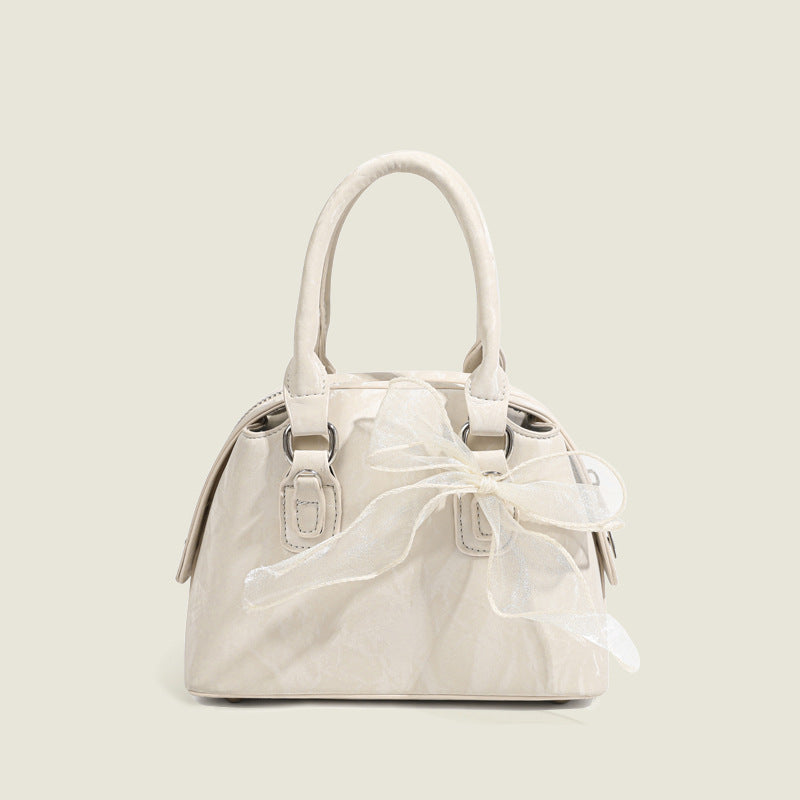 Small structured Boston bag in cream with glossy crinkled finish, sheer bow accent, silver-tone hardware, dual top handles