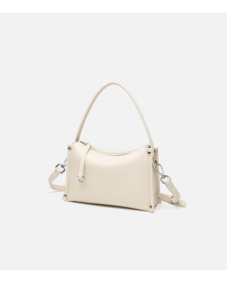Small structured pebbled-finish convertible bag with silver corner studs, zip top, and detachable shoulder strap, detail view