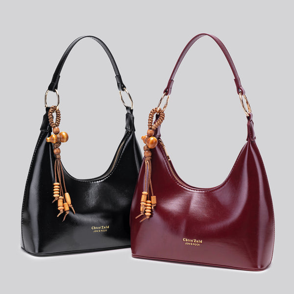 Glossy crescent hobo shoulder bag in deep burgundy with beaded wood tassel charm and gold-tone ring hardware, detail view 2