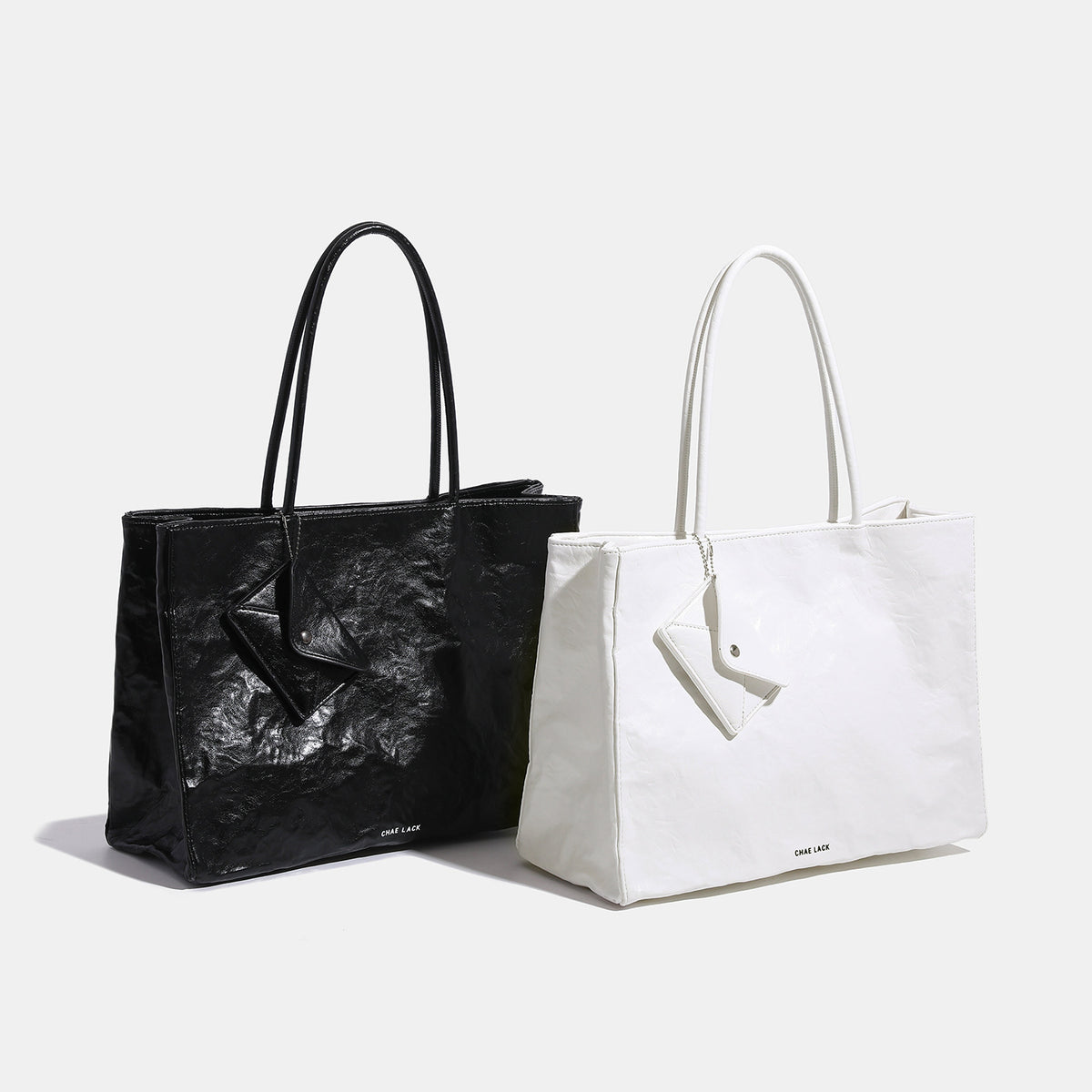 Structured rectangular crinkle leather-look tote bag with long rounded handles, zip top, and envelope-style hanging tag