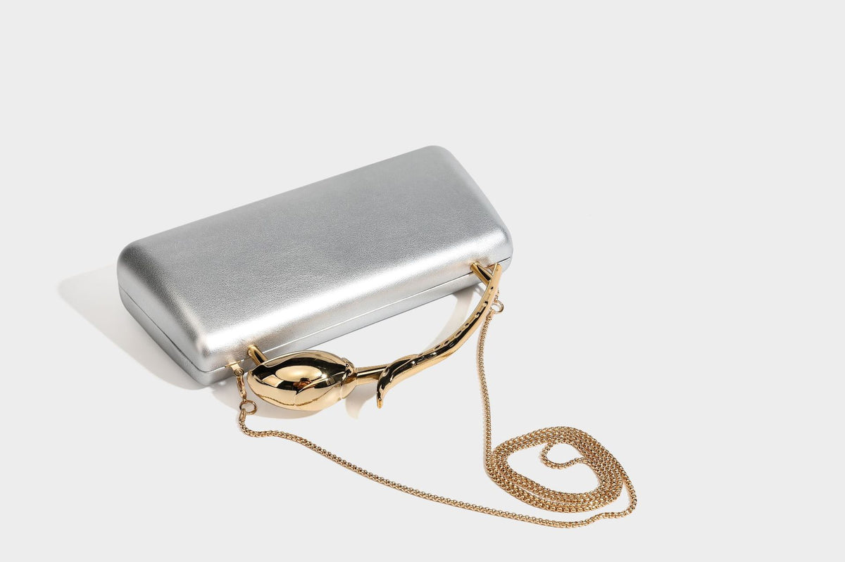 Strukturierte rechteckige Clutch mit goldfarbenem Henkel in Form einer Rosenknospe und abnehmbarem Kettenriemen in Metallic-Optik, Detailansicht