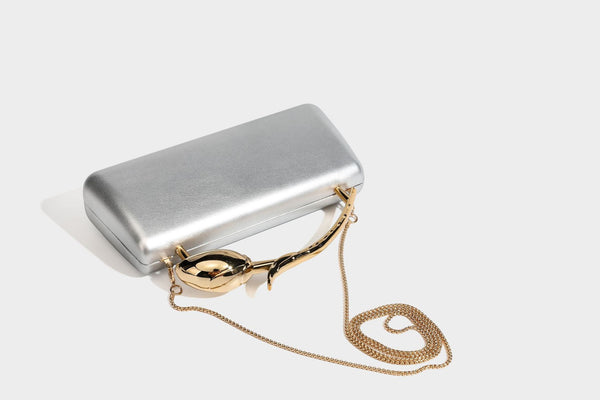 Strukturierte rechteckige Clutch mit goldfarbenem Henkel in Form einer Rosenknospe und abnehmbarem Kettenriemen in Metallic-Optik, Detailansicht