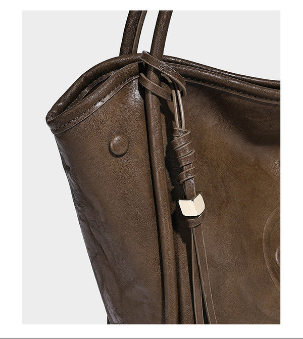 Glänzende Tragetasche in geknautschtem Lederlook mit geprägtem kreisförmigem Emblem, Quastenverschluss, zwei Tragegriffen und abnehmbarem