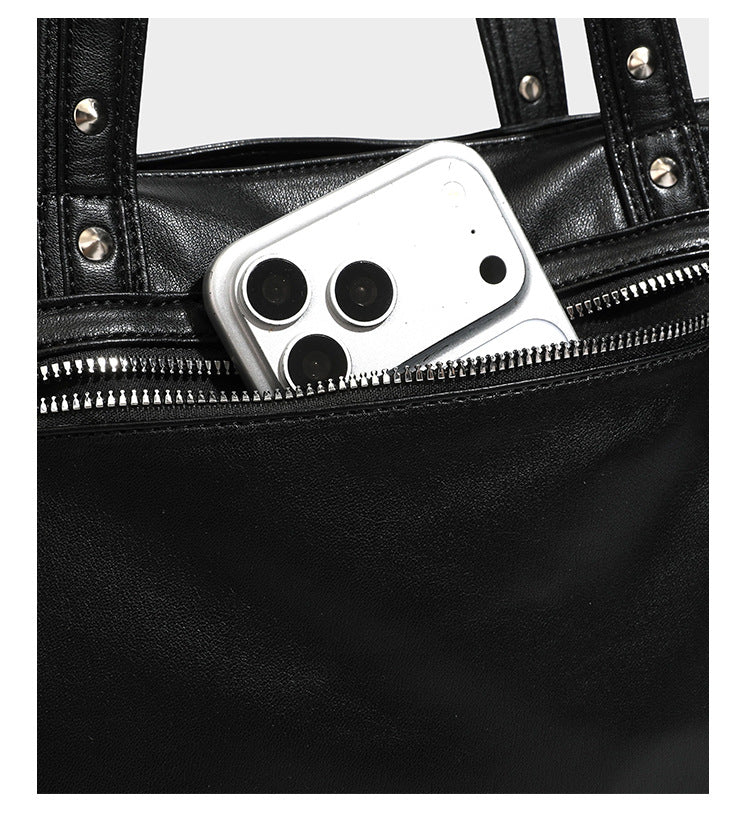Black leather-look tote bag with silver pyramid studs on handles and front panel, multiple flap and zip exterior pockets