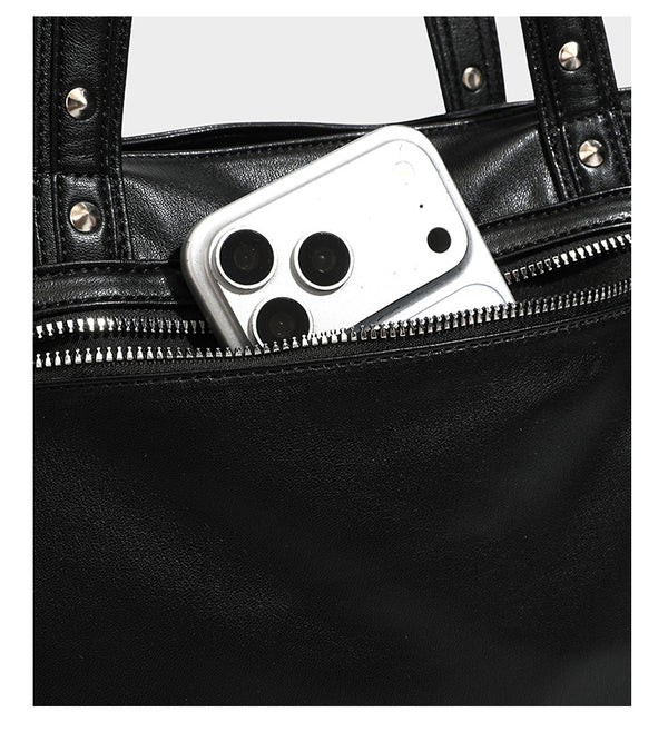Black leather-look tote bag with silver pyramid studs on handles and front panel, multiple flap and zip exterior pockets