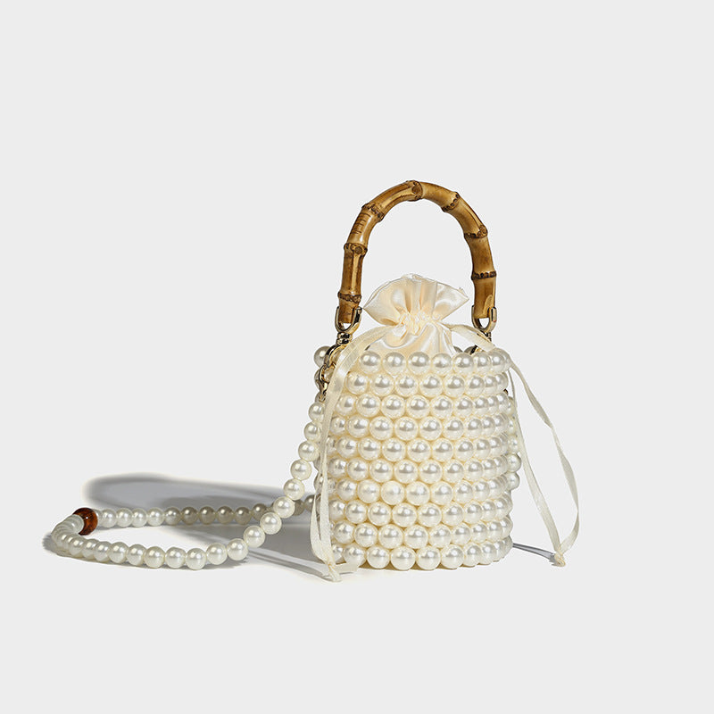 Small cylindrical bucket bag with glossy faux-pearl bead exterior, bamboo arched top handle, satin drawstring closure, and