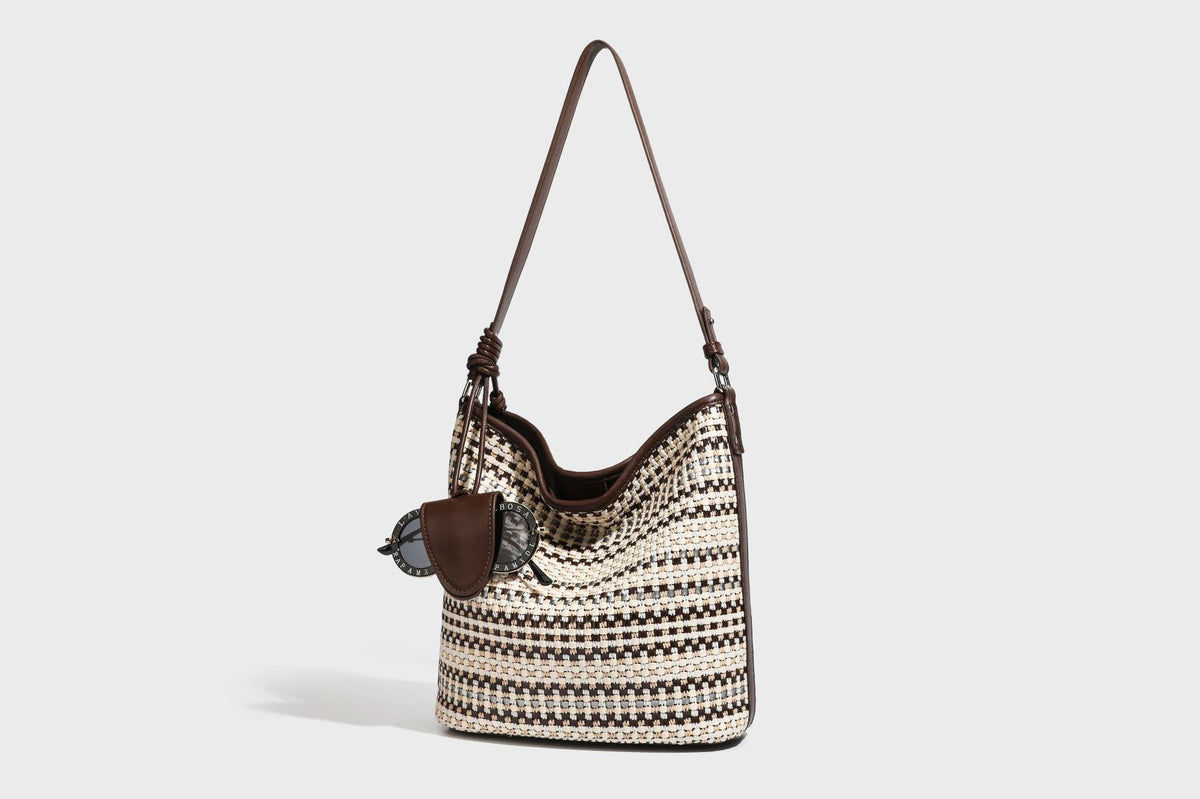 Woven stripe bucket shoulder bag in cream and dark brown with leather-look trim, knotted adjustable strap, and small shield