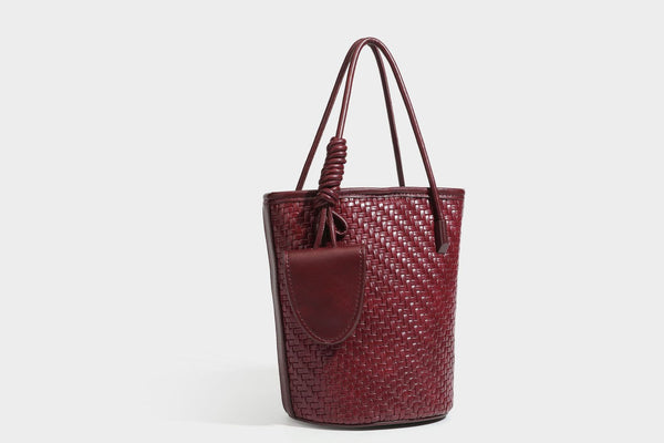 Structured woven-texture leather-look bucket bag in brown with knotted top handles, small front flap pouch, and adjustable