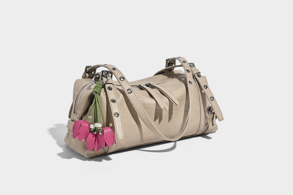 Pale yellow leather-look barrel bag with silver grommet-studded shoulder straps, top zip closure, and pink tulip floral