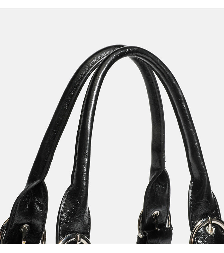 Compact black glossy leather-look satchel bag with silver-tone rivets, buckle hardware, and dual padded top handles, detail