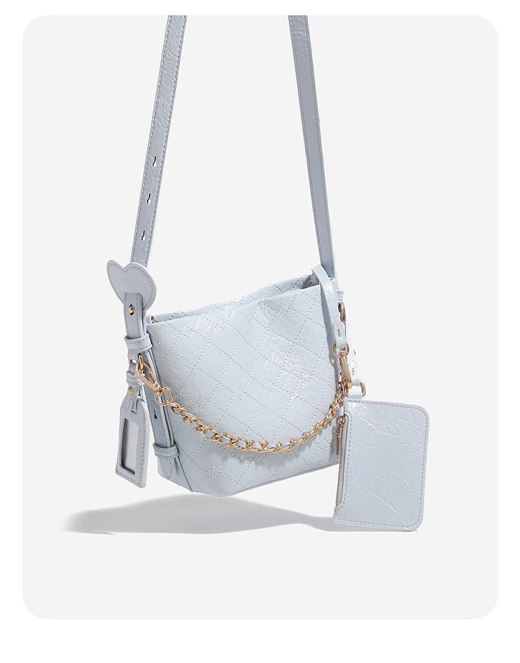 Small diamond-quilted bucket bag with gold-tone chain accent, heart strap detail, hanging tag, and matching zip coin pouch