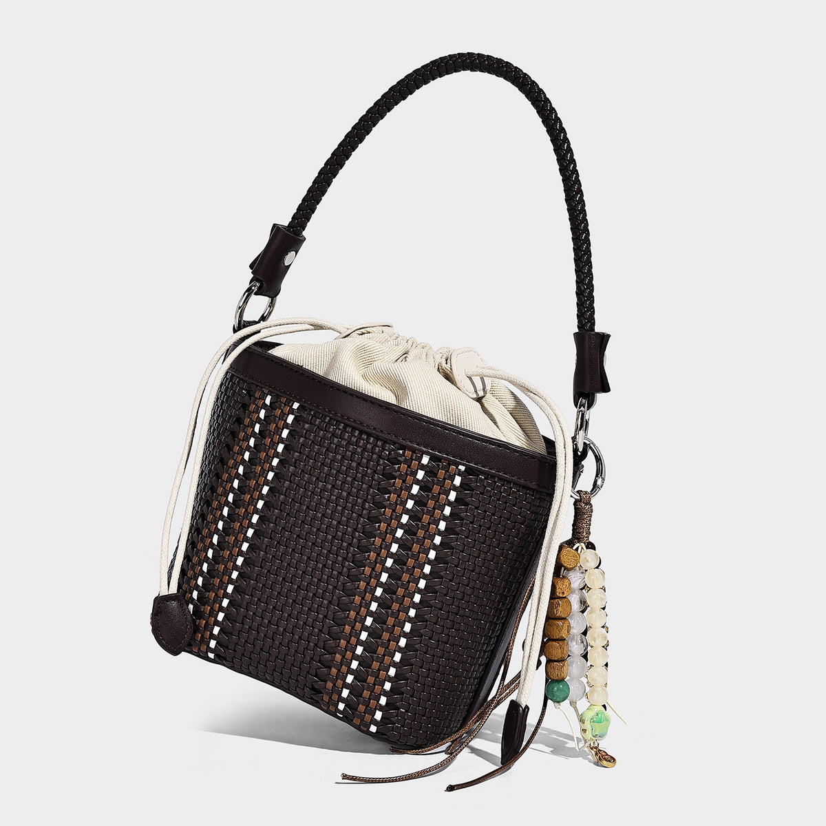Small woven bucket bag with drawstring top, braided handle, detachable crossbody strap, and silver-tone ring hardware, detail