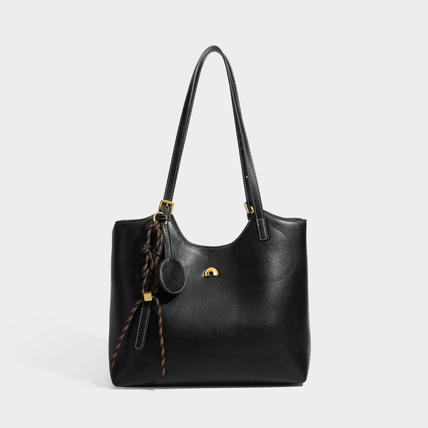 Structured smooth leather-look tote bag with long shoulder strap, gold-tone hardware, and hanging tassel-coin charm, detail