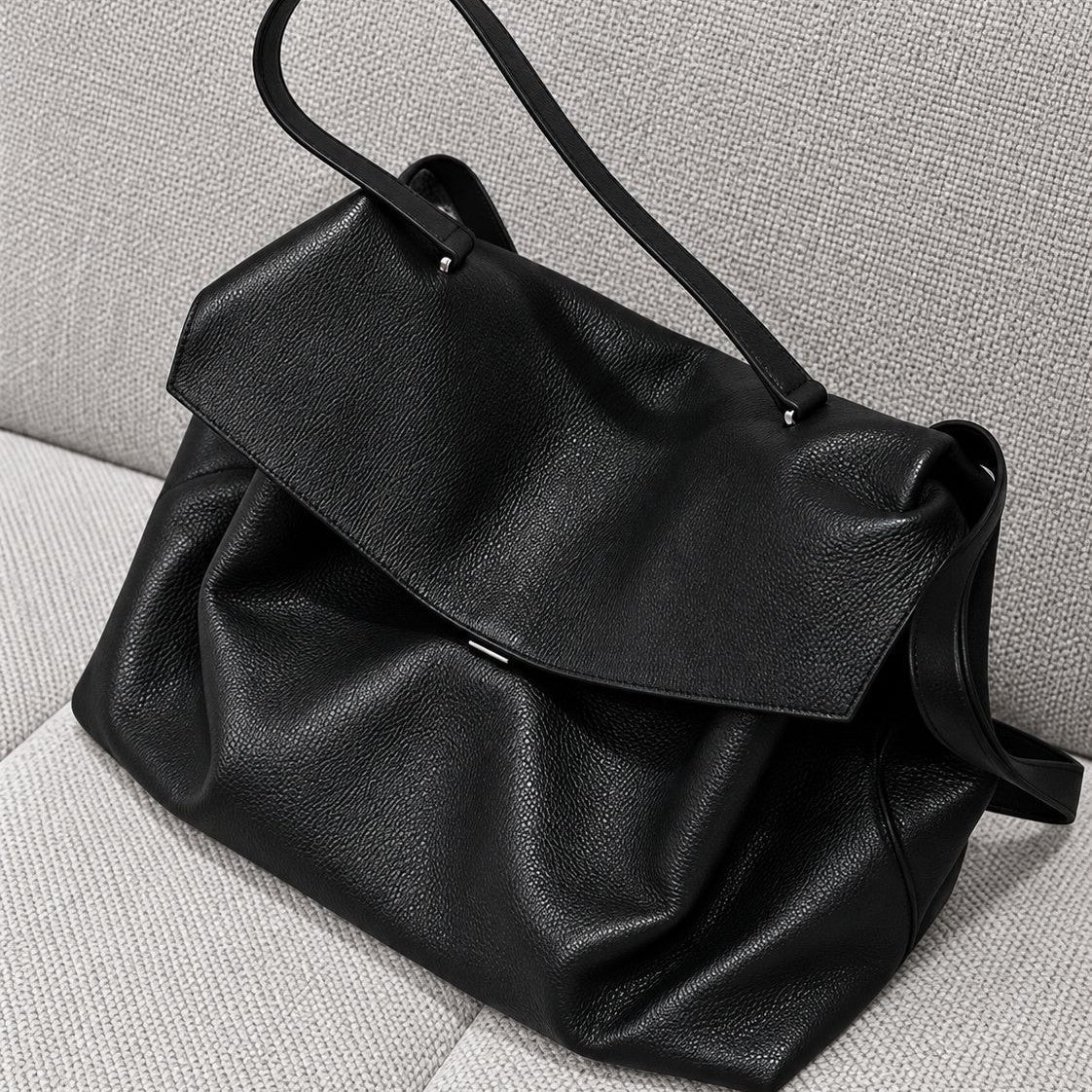 Large black slouchy leather-look shoulder bag with V-shaped envelope flap, silver-tone clasp, and adjustable strap, detail