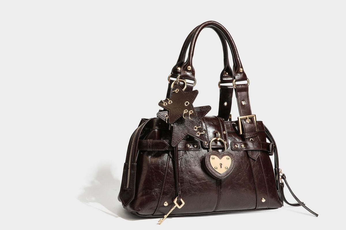 Structured leather-look satchel bag with heart padlock charm, star charm, gold-tone buckle hardware, dual top handles, and