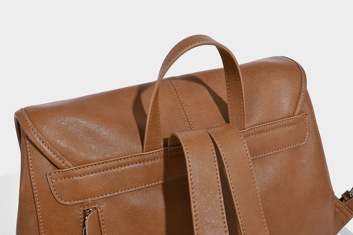 Structured tan leather-look flap backpack handbag with top handle, silver buckle hardware, and fold-over front closure