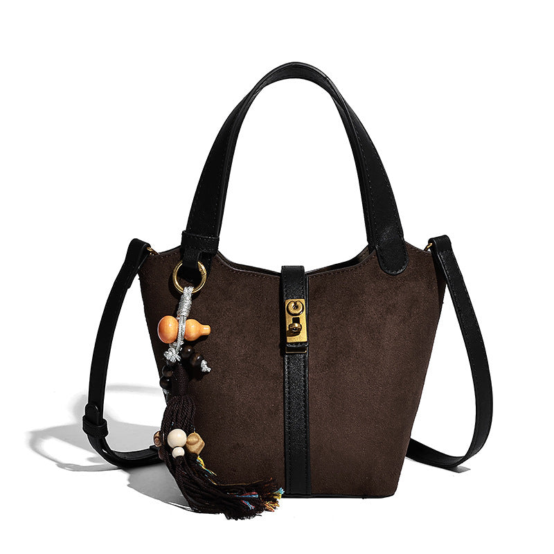 Small structured trapezoid tote bag in matte suede-look finish with black contrast trim, gold-tone front clasp, tassel charm