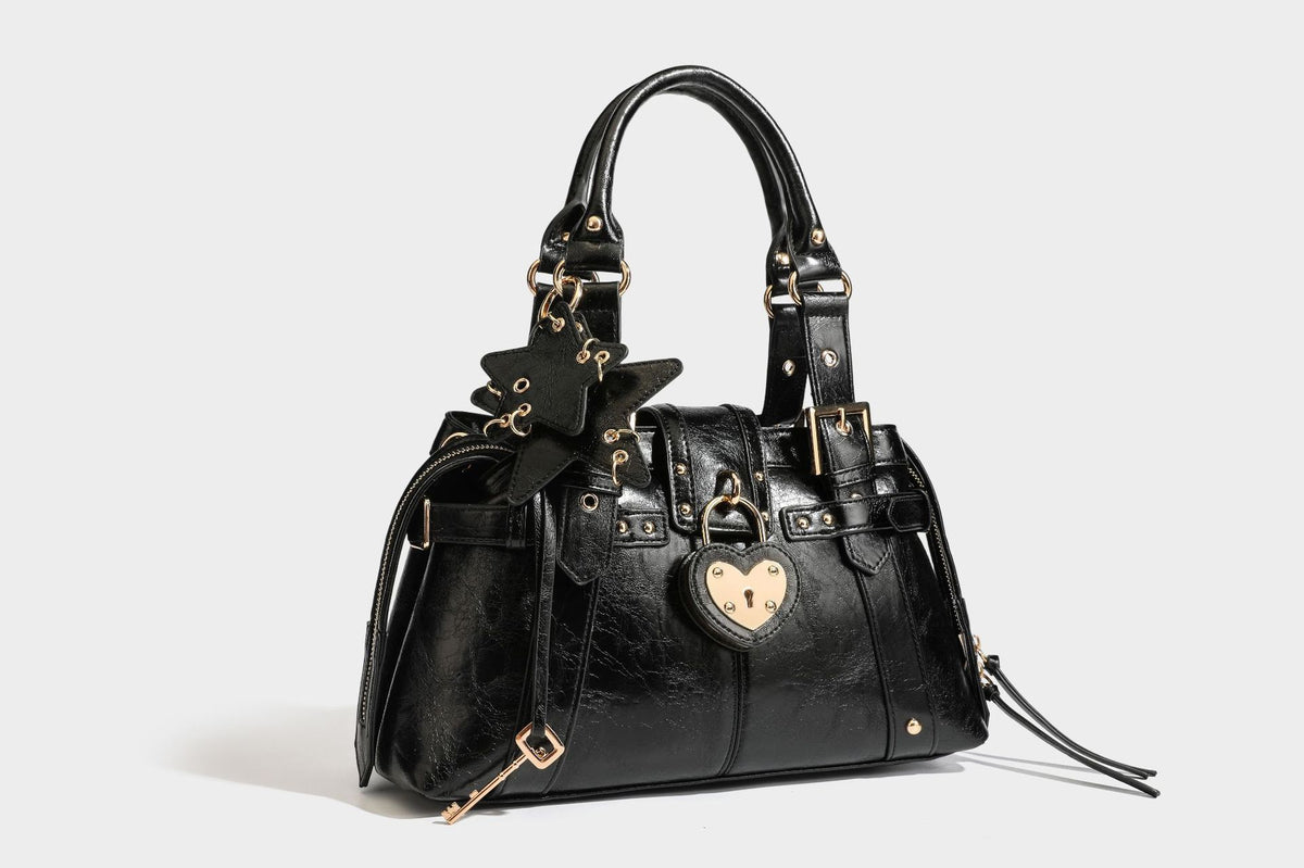 Structured leather-look satchel bag with heart padlock charm, star charm, gold-tone buckle hardware, dual top handles, and