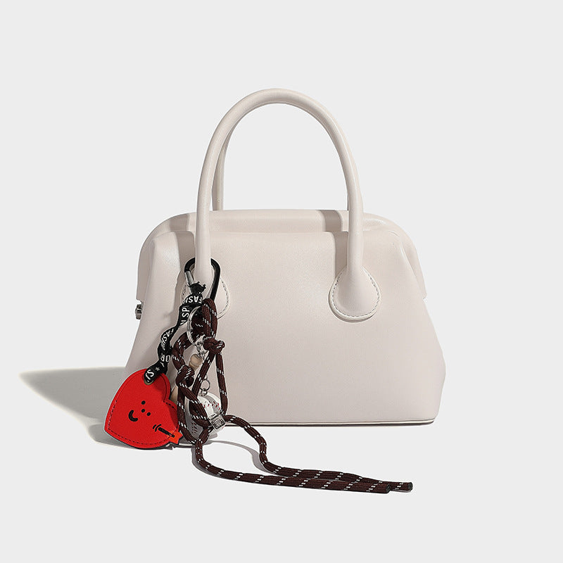 Small structured shell top-handle bag in red with heart charm and braided cord detail, smooth leather-look finish, detail