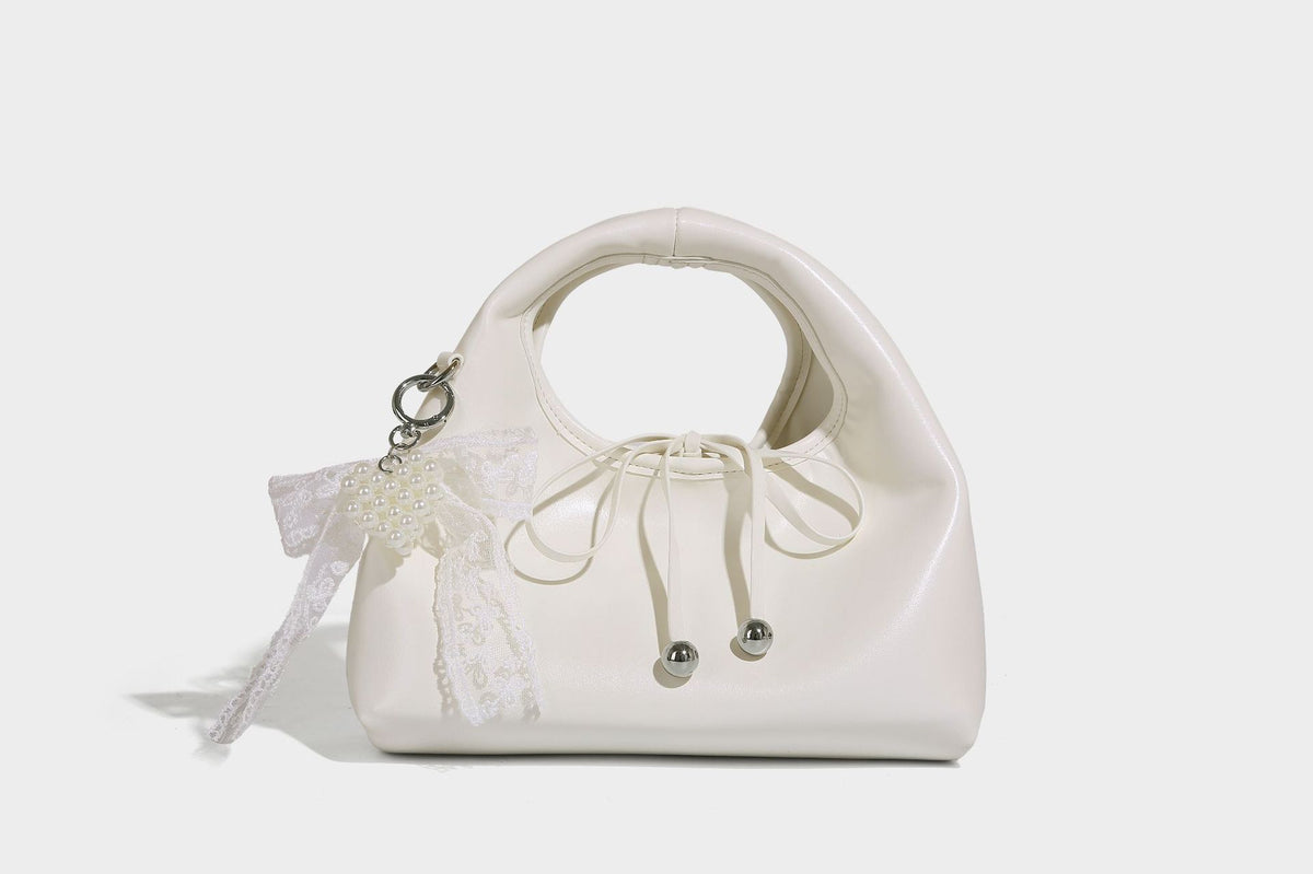 Kleine kuppelförmige Henkeltasche in glänzender Lederoptik mit Kordelzugverschluss, weißem Spitzen-Schleifenanhänger und silberfarbenen Metallbeschlägen