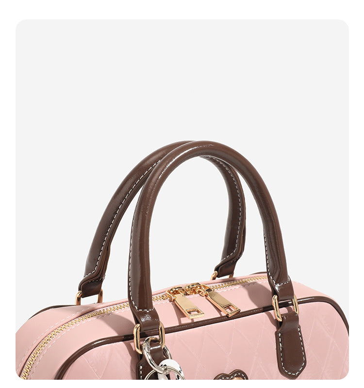 Blush pink quilted bowling barrel bag with dark brown leather-look trim and handles, baseball bat and ball charm, gold-tone