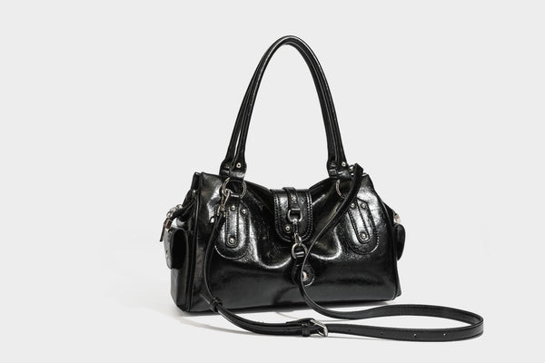Glänzende, geknautschte Barrel-Satchel mit zwei oberen Tragegriffen, vorderem Klappen-Riemen-Panel, Ring- und Nietenbeschlägen sowie einem abnehmbaren