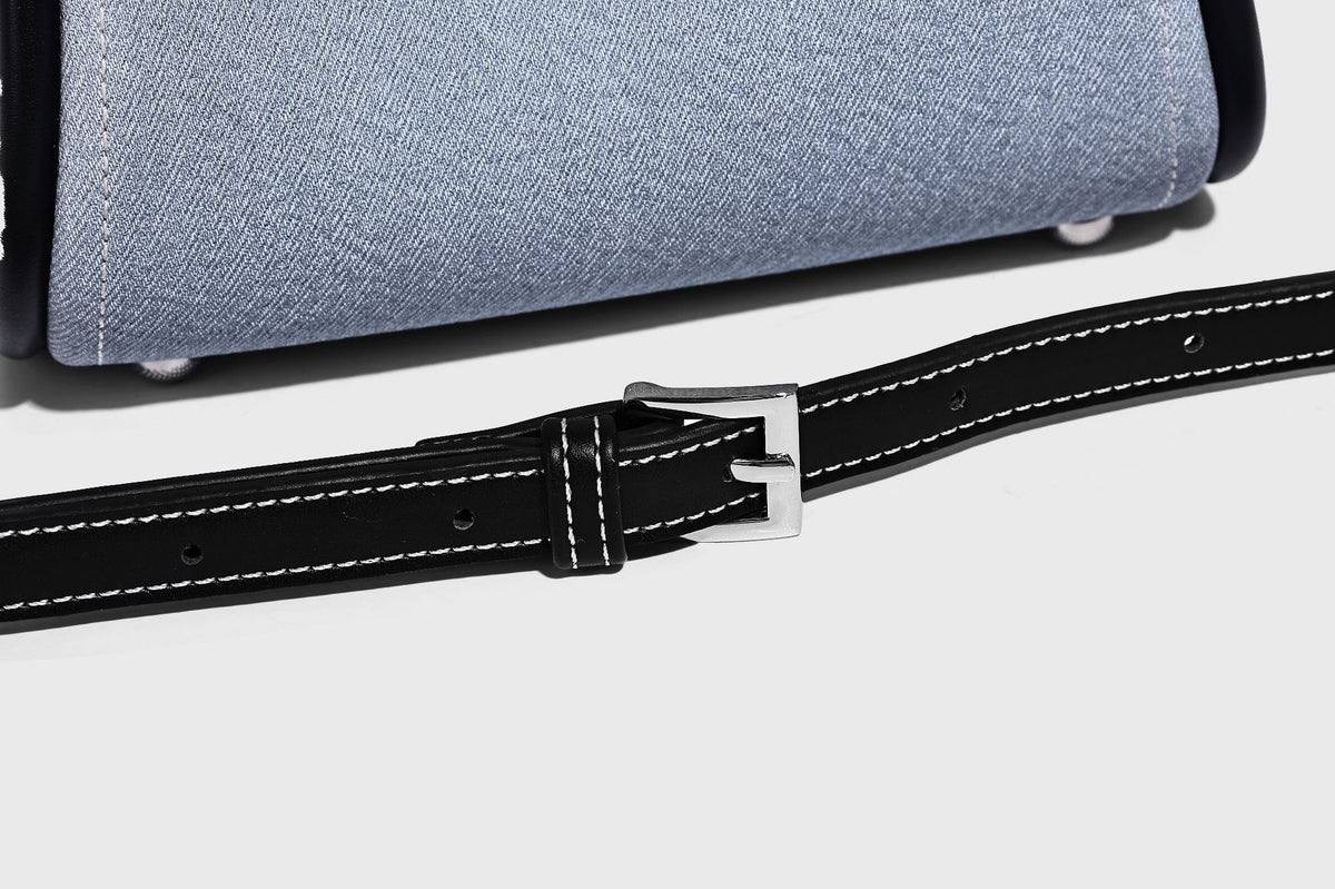 Light blue denim trapezoid tote bag with black leather-look trim, knotted top handles, detachable crossbody strap, front