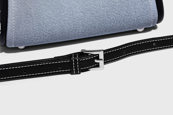 Light blue denim trapezoid tote bag with black leather-look trim, knotted top handles, detachable crossbody strap, front