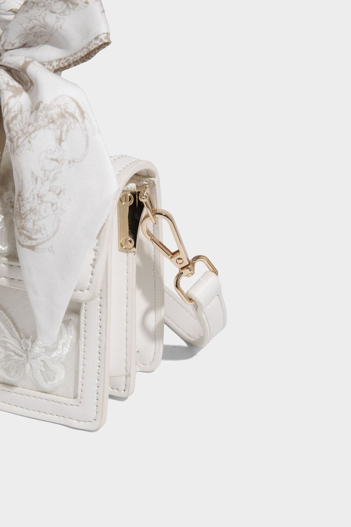 Small structured white flap bag with butterfly embroidery, flower-shaped turn-lock clasp, braided top handle with scarf bow