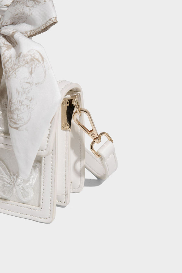 Small structured white flap bag with butterfly embroidery, flower-shaped turn-lock clasp, braided top handle with scarf bow