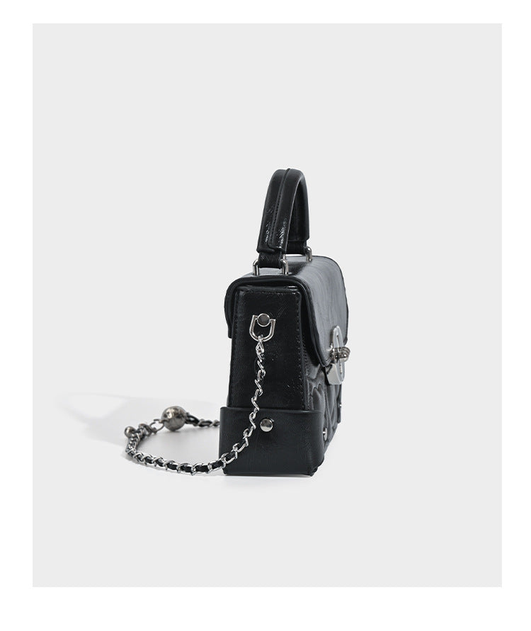 Kleine strukturierte Box-Tasche aus herzförmig gestepptem PU mit Henkel, silberfarbenem Kettenriemen zum Tragen als Crossbody und ovalem Drehverschluss, Detailansicht