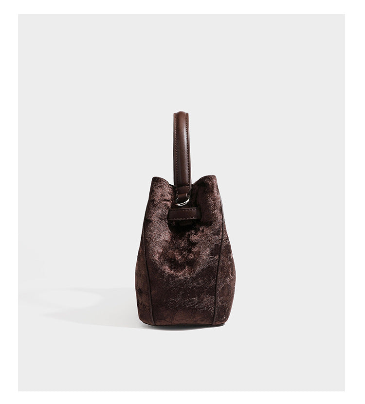 Small structured bucket satchel in embossed velvet-texture fabric with silver turn-lock hardware, rounded top handle, and