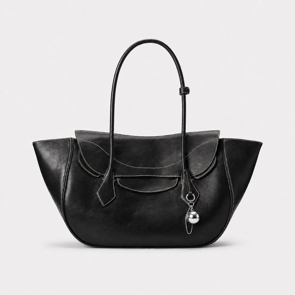 Large winged leather-look tote bag with single arched handle, stitched flap-front panel, and silver ball charm in cognac