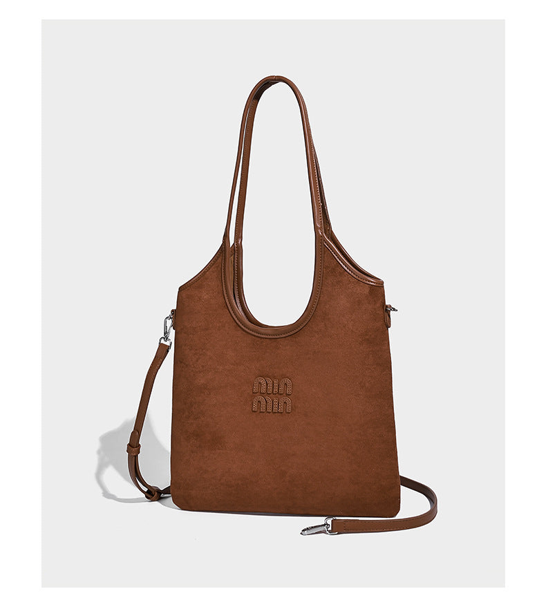 Tote-Bag in warmem Braun mit matter Wildlederoptik, langen Tragegriffen, geprägtem Logo, silberfarbenen Beschlägen und passendem, Detail