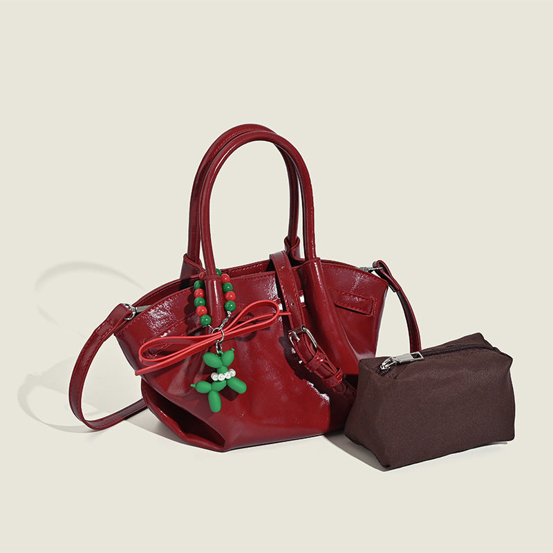 Small structured red glossy PU handbag with bow-and-bead charm, dual top handles, and detachable crossbody strap, detail view
