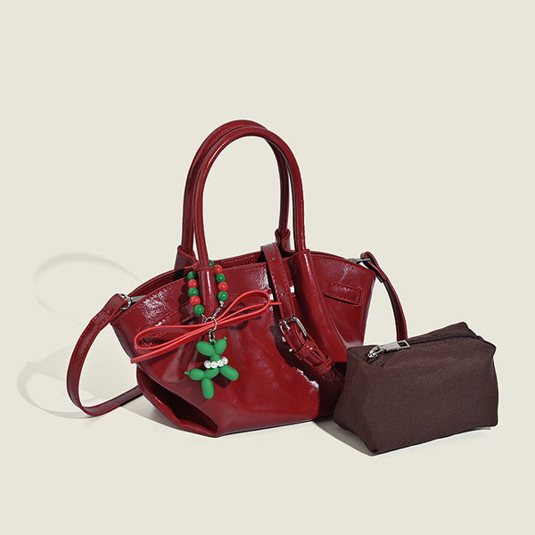 Small structured red glossy PU handbag with bow-and-bead charm, dual top handles, and detachable crossbody strap, detail view