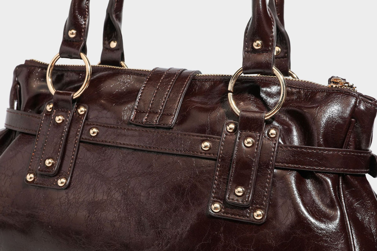 Glänzende Henkeltasche in Lederoptik mit zwei Tragegriffen, goldfarbenen Nieten und Ringen, dekorativem Schnallriemen auf der Vorderseite und