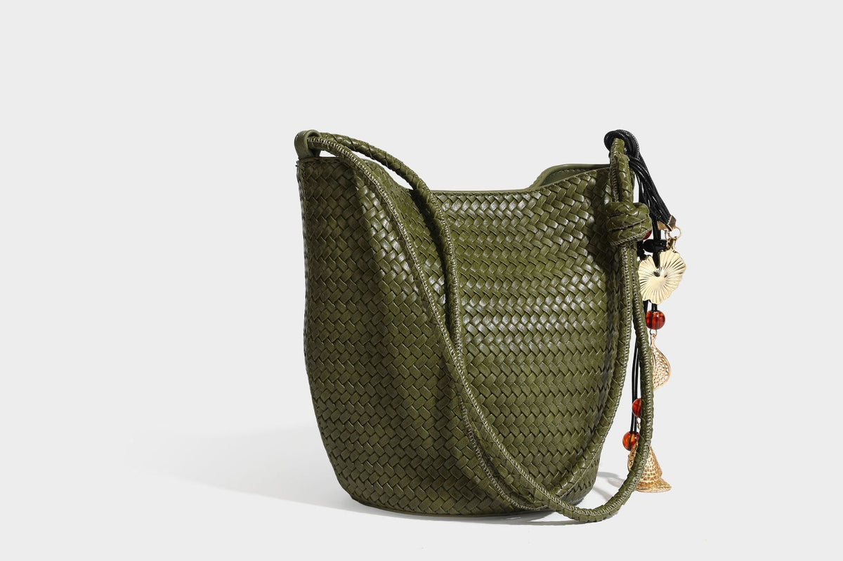 Olive green woven leather-look bucket bag with braided crossbody strap, knotted adjustment, and gold-tone tassel charm with