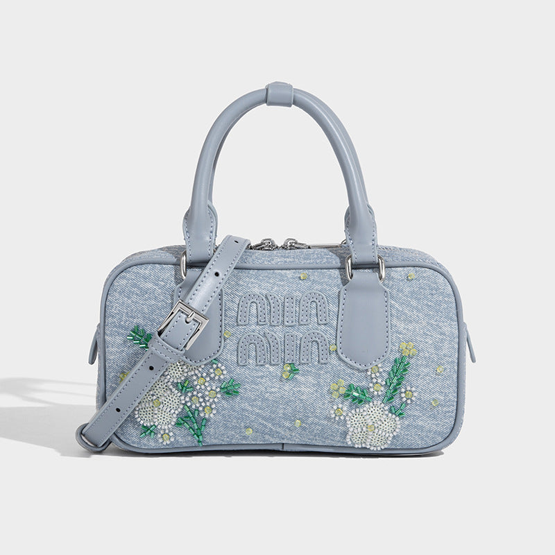 Small light blue denim-look barrel bag with white floral bead embroidery, dual top handles, and detachable shoulder strap