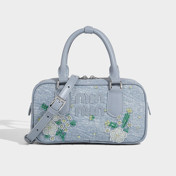 Small light blue denim-look barrel bag with white floral bead embroidery, dual top handles, and detachable shoulder strap